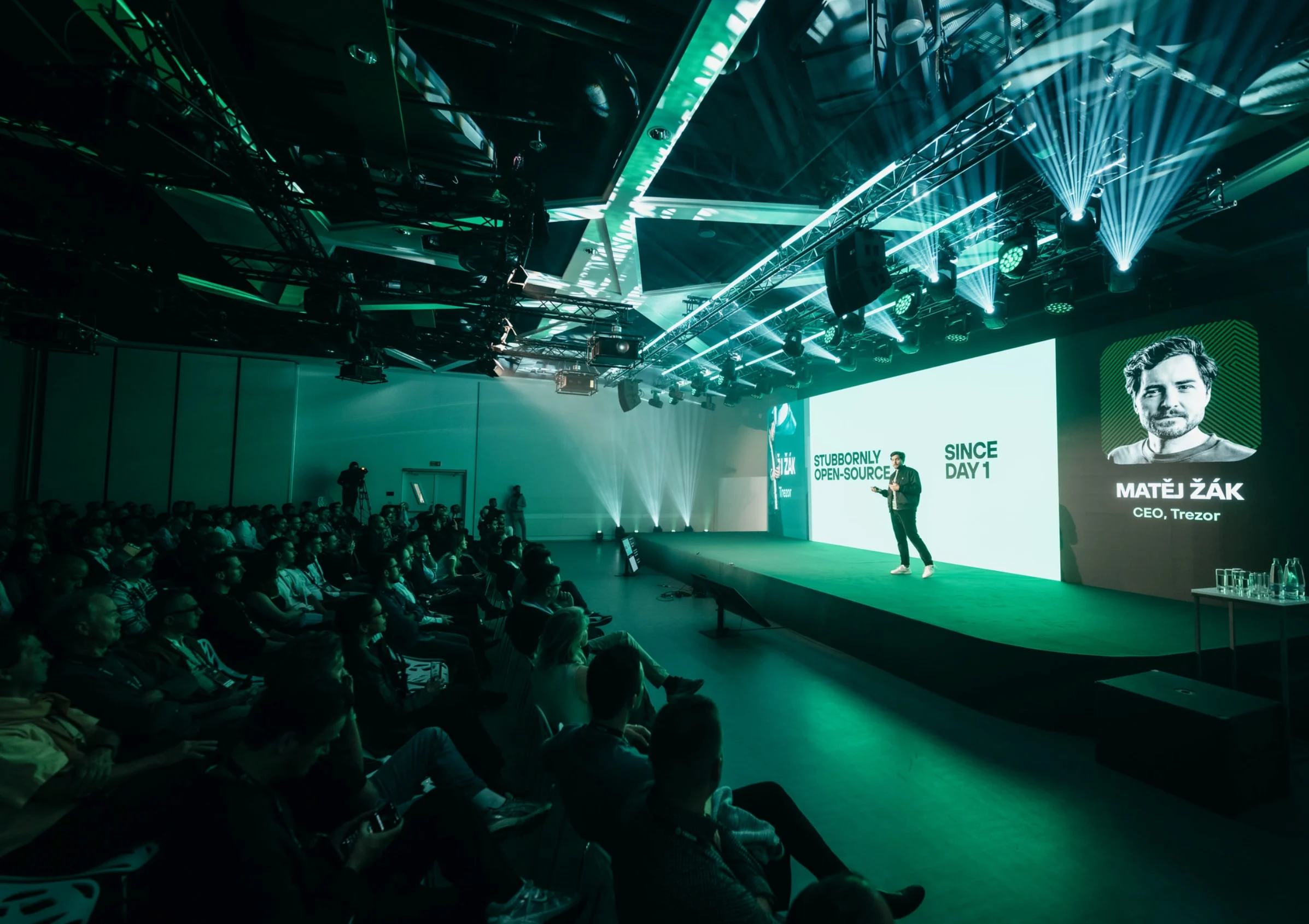 A speaker on stage at the Trezor Safe 7 launch keynote, a large screen behind him reading “Matej Zak, CEO”.