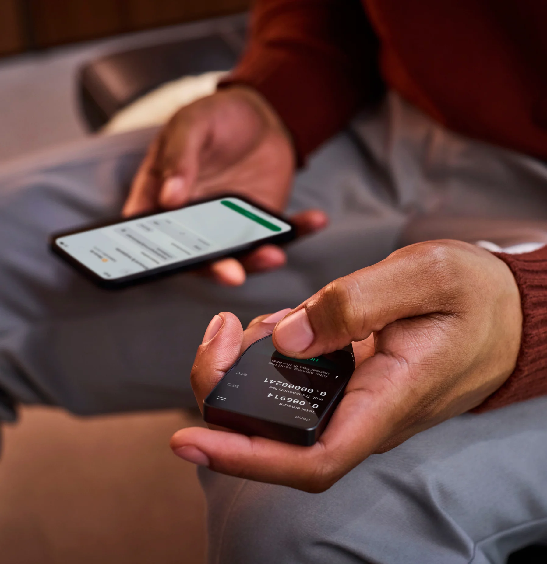 Close-up of hands holding a phone and a Trezor device to confirm a transaction.