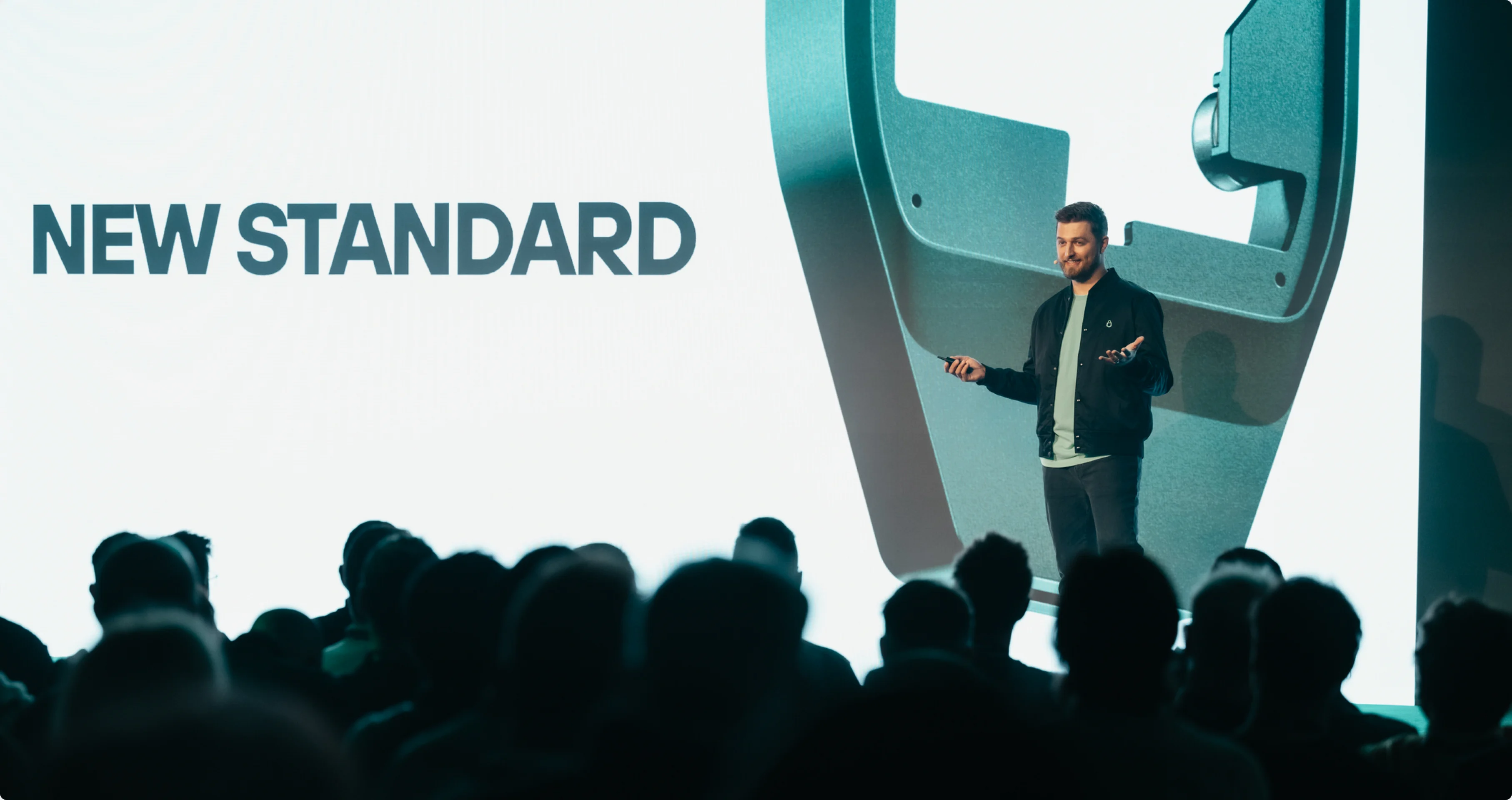 The keynote stage — “New standard” on screen above a silhouetted audience.