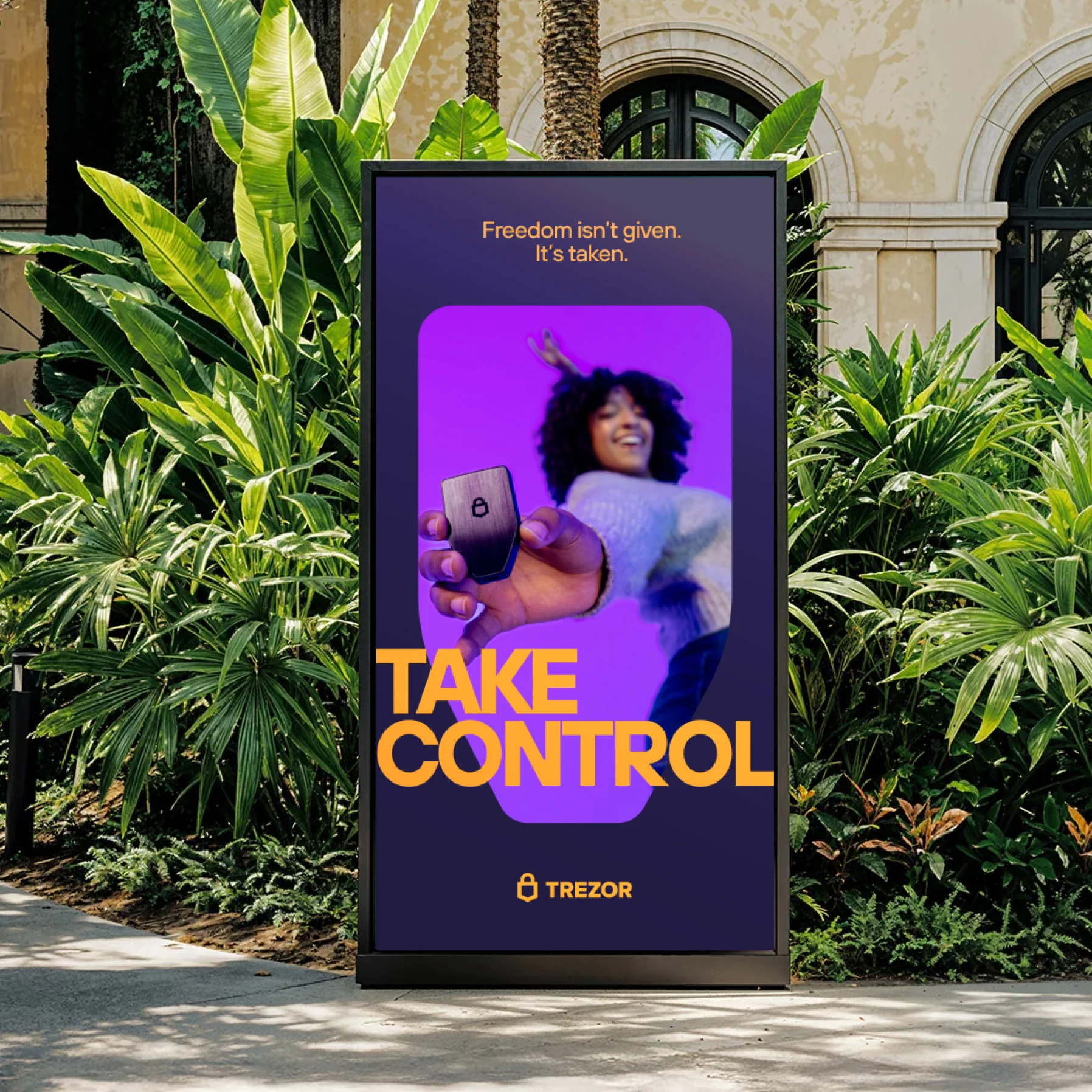 A “Take control / Freedom isn't given. It's taken.” digital billboard among tropical plants.